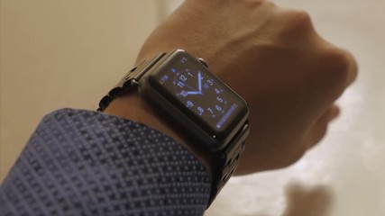 Poster - Man hand in watch with program on the screen against the background of table. Man hand at the home with watch and app on the screen. Modern smart watch with cloud of apps