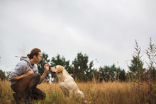 A Man Sitting With Dog In Fall Field