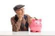 Pensive senior with a piggybank seated at a table