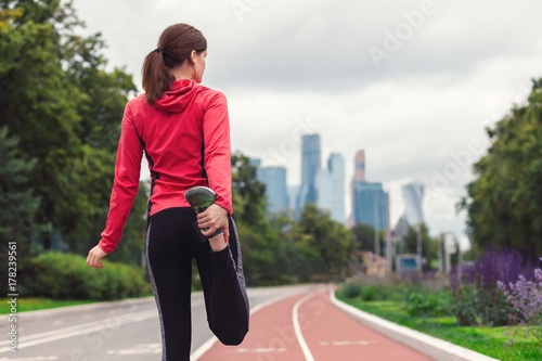 Plakat młody biegacz dziewczyna fitness rozciąga nogi przed uruchomieniem w mieście