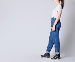 Wall Mural - Woman wearing casual outfit with white t-shirt, blue high-waisted mom jeans with black faux leather ankle boots and black belt isolated on grey background. Copy space