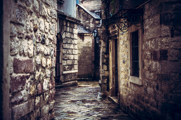 Dark vintage medieval narrow winding street with ancient stone building facade with medieval architecture in old european city Kotor in Montenegro 