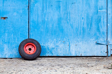 Minimalist Image Of A Red Wheel Leaning Against A Blue Door
