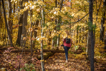 woman hiking through woods in autumn with camera