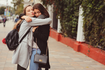 two young happy girlfriends walking on city streets in casual fashion outfits, wearing warm coats and having fun