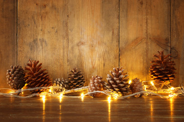 Holiday image with Christmas golden garland lights and pine cones over wooden background