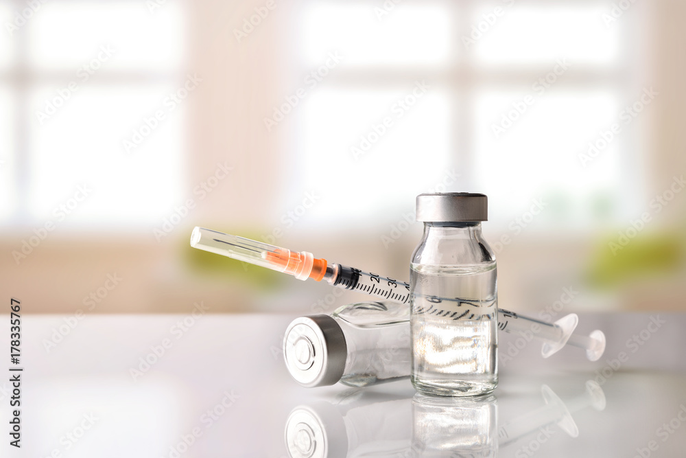 Vials and syringe on white table with background windows - obrazy, fototapety, plakaty 
