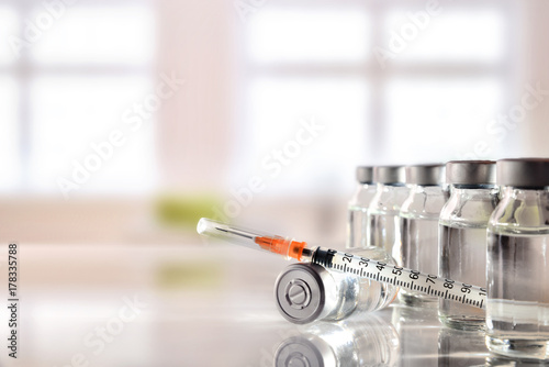 Fotografía Vials group and syringe on white table with background windows