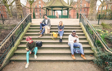 Wall Mural - Group of multiracial friends using mobile smart phone sitting on stairs at park - Young hipster people addicted by smartphone on social network community - Technology concept - Desaturated color tones