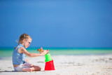 Fototapeta Pomosty - Little girl at tropical white beach making sand castle