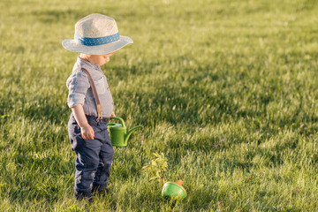 Wall Mural - Toddler child outdoors. One year old baby boy wearing straw hat using watering can