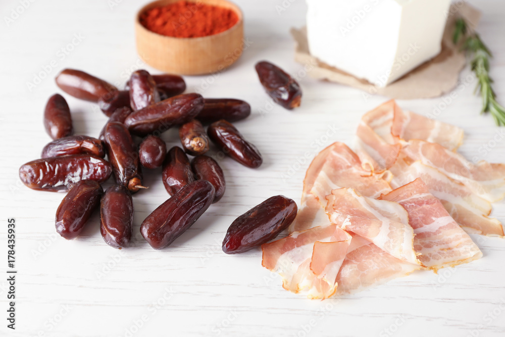 Ripe dates and raw bacon strips on light background