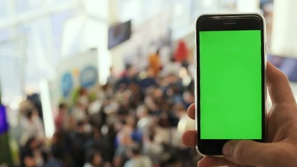 right hand using smart phone green blank screen blur background closeup people group meeting convention hall chromakey mockup tapping touchscreen point rate business technology trade 3g app wifi