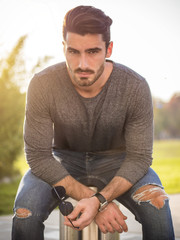 Wall Mural - Attractive young bearded man portrait sitting outside in urban environment