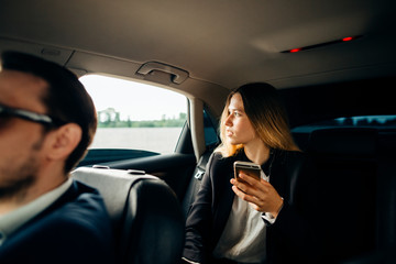 business woman using smart phone and smiling while sitting on back seat in car