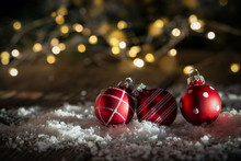 Three Red Baubles In Front Of Lights On Snow And Wooden Ground