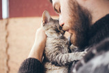 Fototapeta Koty - Cat and man, portrait of happy cat with close eyes and young man, people playing with the kitten. Handsome Young Animal-Lover Man, Hugging and Cuddling his Gray Domestic Cat Pet