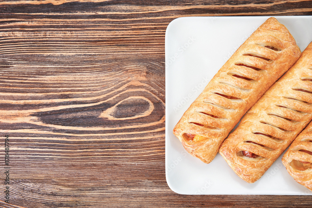 Plate with tasty sausage rolls on wooden table