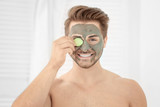 Fototapeta  - Young man with cosmetic mask on his face in bathroom