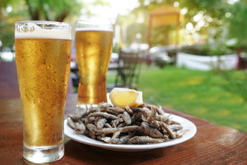 Wall Mural - Glasses of fresh beer and plate with yummy fried anchovies on wooden table outdoors