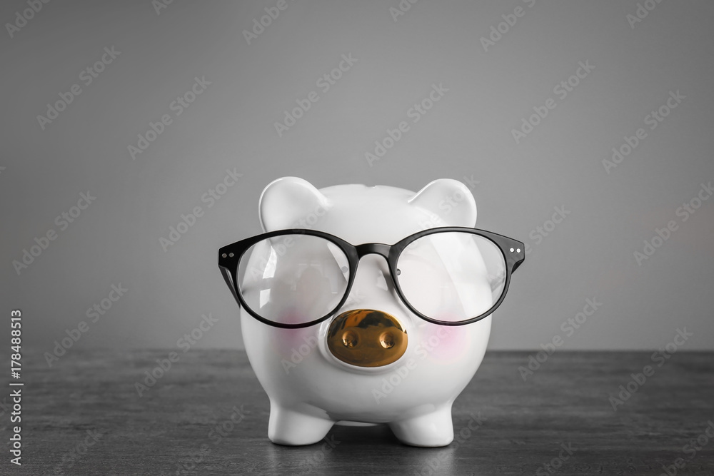 Cute piggy bank with glasses on table against grey background