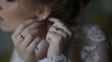 Beautiful bride in puts on earring. Beauty model girl is wearing jewelry for marriage. Wedding female portrait. Woman with curly hair and lace veil. jewelry and beauty concept - close up of wearing