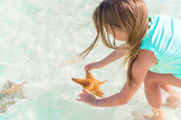 Adorable little girl with starfish on white empty beach