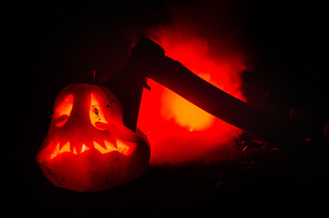 Wall Mural - Scary orange pumpkin with carved eyes and a smile with burning candles and an ax on a dark background with fire sky. For the Halloween party. Empty space.