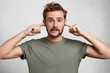 © wayhome.studio - Stressful man with trendy hairdo, mustache and beard plugs ears, avoids loud sounds at street, doesn`t want to listen noise, isolated over white background. Bearded man ignores something unpleasant