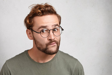 Wall Mural - Is it so? Curious surprised young atrractive man with beard and mustache, curves lips, looks in bewilderment as tries to understand very difficult material or information. Hipster gazes in puzzlement