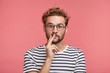© wayhome.studio  - Headshot of stylish man with trendy hairdo, wears round spectacles, keeps fingers on lips, has shocked expression, don`t expect to see his companion at home, didn`t wait for guests, not prepared