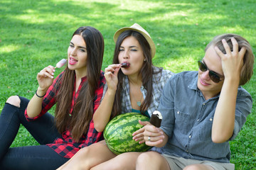 Wall Mural - Young man and women eating chocolate ice-cream and watermelon outdoor in summer park. Friends have fun outdoor. Leaisure, youth, summertime.