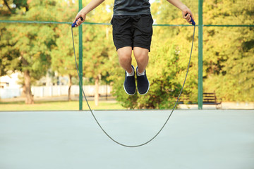 Young sporty man jumping rope outdoors