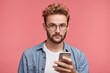 © WHstudio Leushin N - Serious stylish youngster with trendy hairstyle holds smart phone in hands, uses free internet connection, surfes social networks or messages with friends, being always in touch or connected