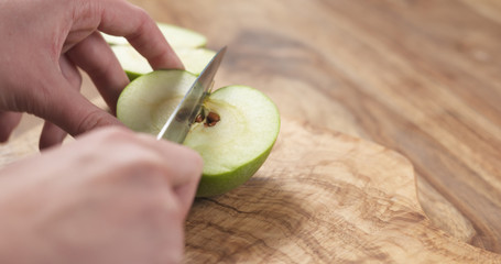 Wall Mural - young female hands cut green apple into quarters