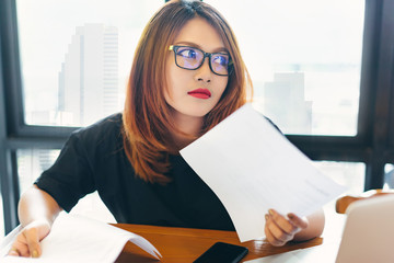 Asian stylish glasses woman designer wear black dress and red lips working with her laptop and checking the document in selective focus..