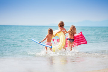 Wall Mural - Three girls with swimming tools running to the sea