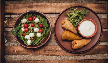 Wall Mural - Tasty meat rolls with sour cream and salad on wooden table