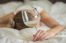 Jovem Mulher Loira Desmaiada Na Cama Após Abusar De Bebidas Alcoólicas, Taça De Vinho Na Mão.