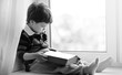 © alexkich - The little boy is reading a book. The child sits at the window a