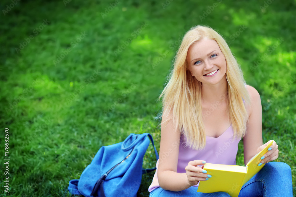 Beautiful young woman reading book while sitting on lawn in park