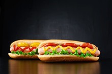 Two Big Hotdog With Sausage Tomatoes, Mustard, Ketchup And Salad Isolated On Black Background. Front View.