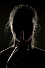 Misterious Portrait Of Woman In Shadow With Finger On Her Lips On Dark Background