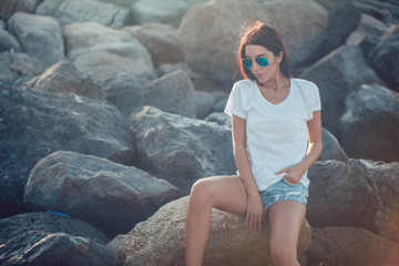 Girl in a white t-shirt and sunglasses on the background of stones. Mock-up.