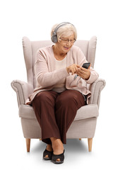 Wall Mural - Elderly woman sitting in an armchair and listening to music on a phone