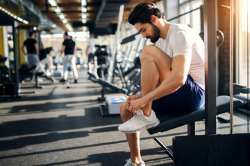 Sticker - Handsome bearded man ties up his shoelaces on sneakers at the gym before exercises.