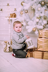 Cheerful little baby boy playing with gifts and presents near Christmas tree, gold and beige pastel c