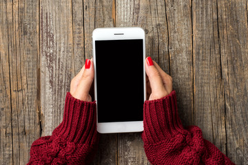 Wall Mural - Female hands in warm sweater holding white smart phone. Close up