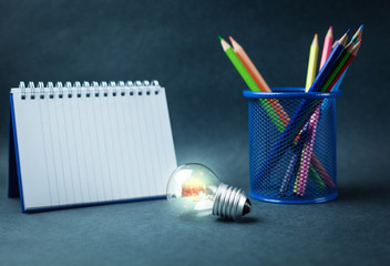 Wall Mural - Light bulb with color pencils and notepad on a blue background.