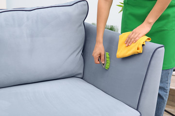 Wall Mural - Woman cleaning couch with brush and duster at home